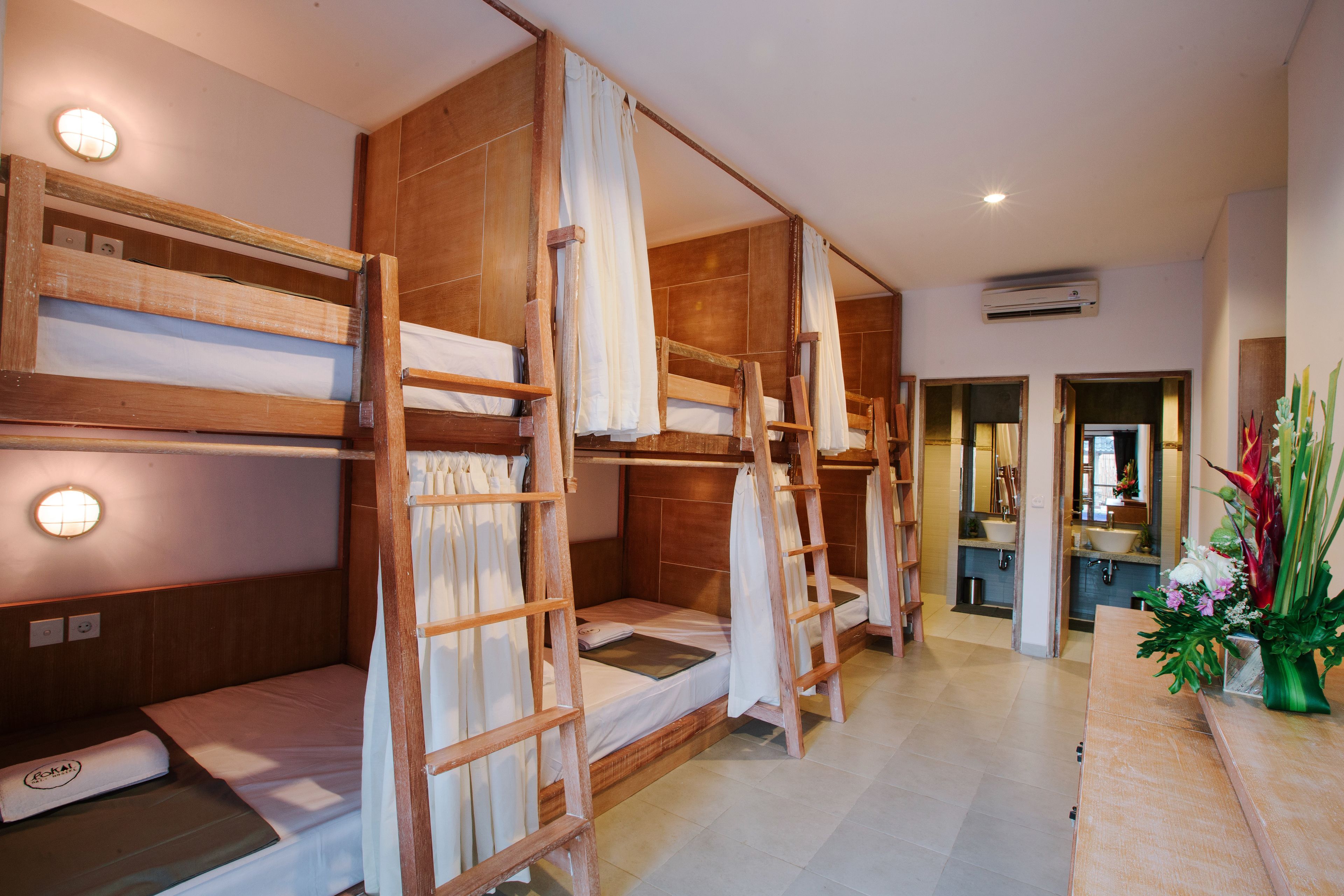 A hotel room with bunk beds, a bathroom with a sink, and a vase of flowers on the counter.