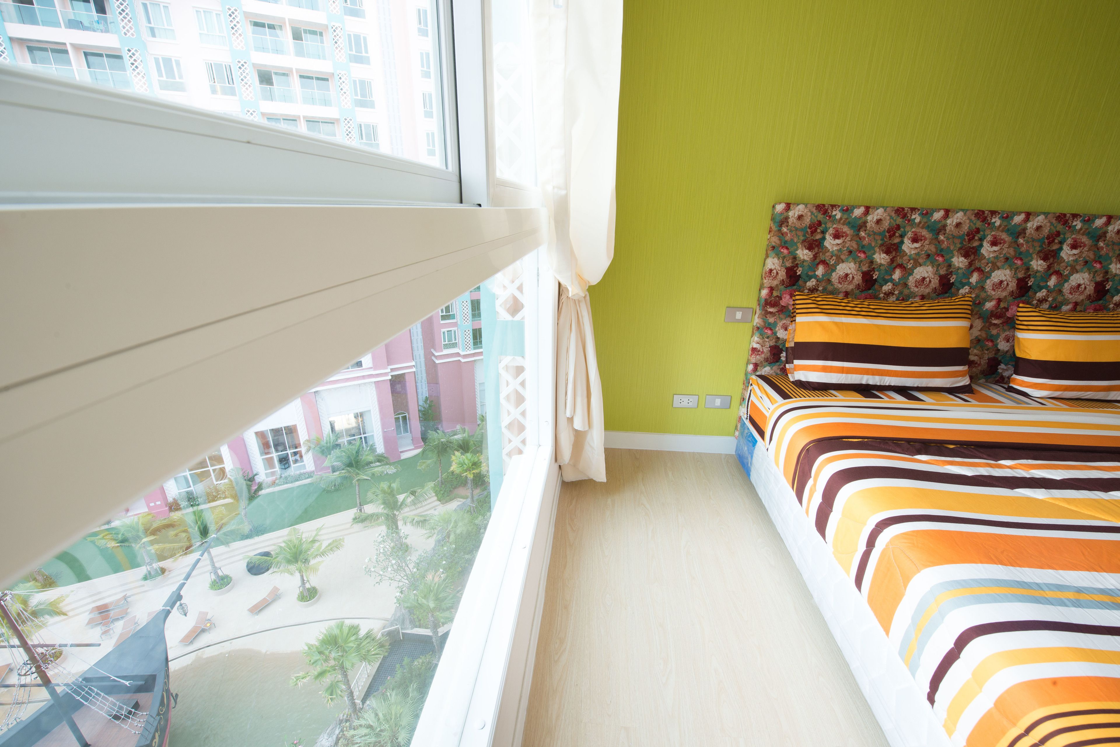 Un dormitorio con vistas a un patio, una cama con ropa de cama a rayas y una ventana con cortinas.