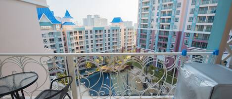 A balcony with a view of high-rise buildings, a pool, and a covered area.
