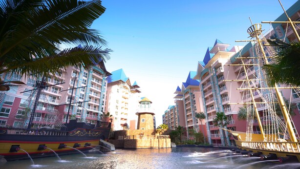 A water fountain with a ship design, surrounded by palm trees and multi-story buildings with balconies. - Grande Caribbean Hotel Resort Pattaya (Pattaya)