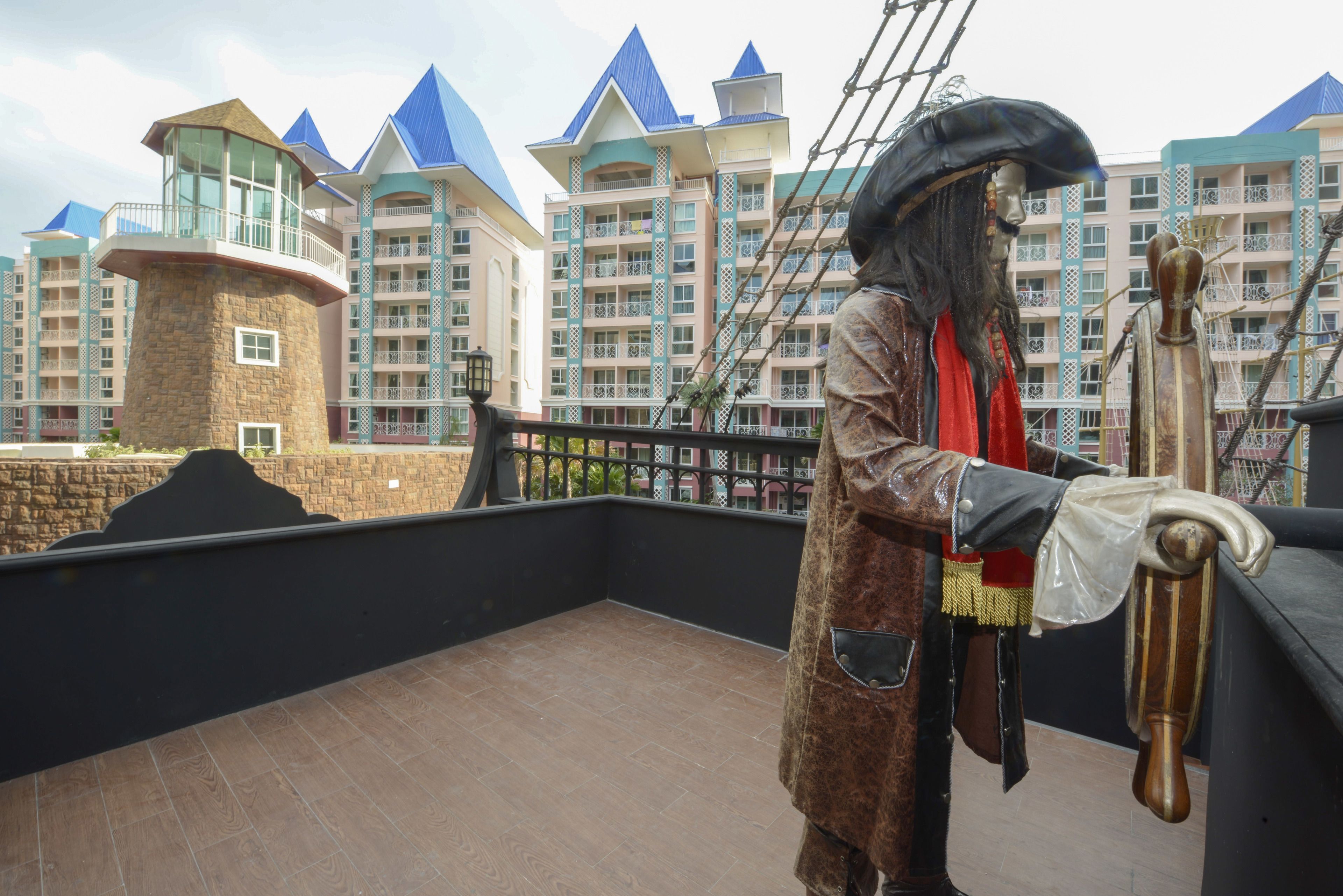 A lifelike pirate statue on a balcony with a view of modern buildings in the background.