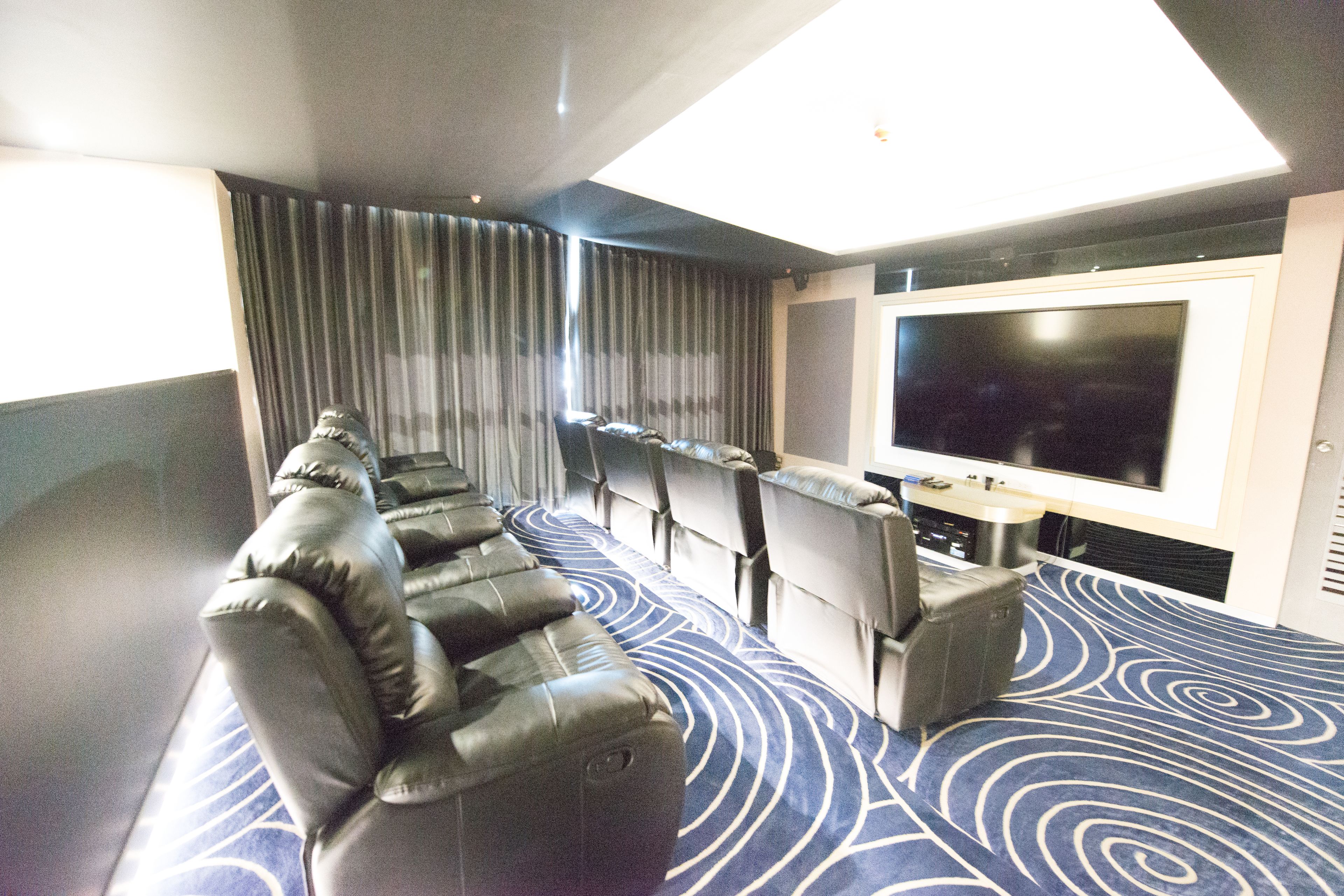 A hotel room with a large flat-screen TV, a row of leather sofas, and a patterned carpet.