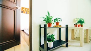 Um corredor com porta de madeira, parede branca e prateleira de metal com plantas em vasos.