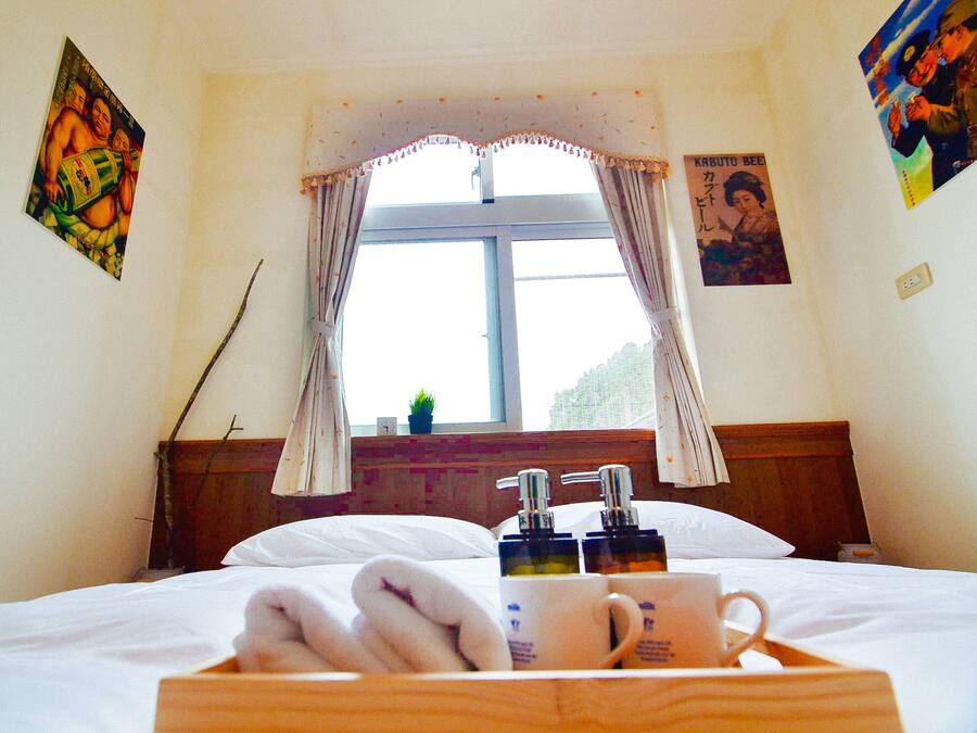 Habitación de hotel con cama, ventana con cortinas, mesita de noche con artículos de aseo y decoración en las paredes.