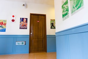 A hallway with a wooden door marked with the number 305, blue wainscoting, and several posters on the walls. - Yahu Hotel (Zhuqi)