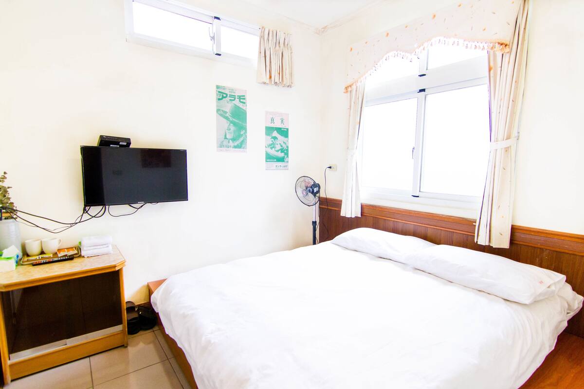 Una habitación de hotel con una cama, televisión, ventilador y ventana con cortinas.