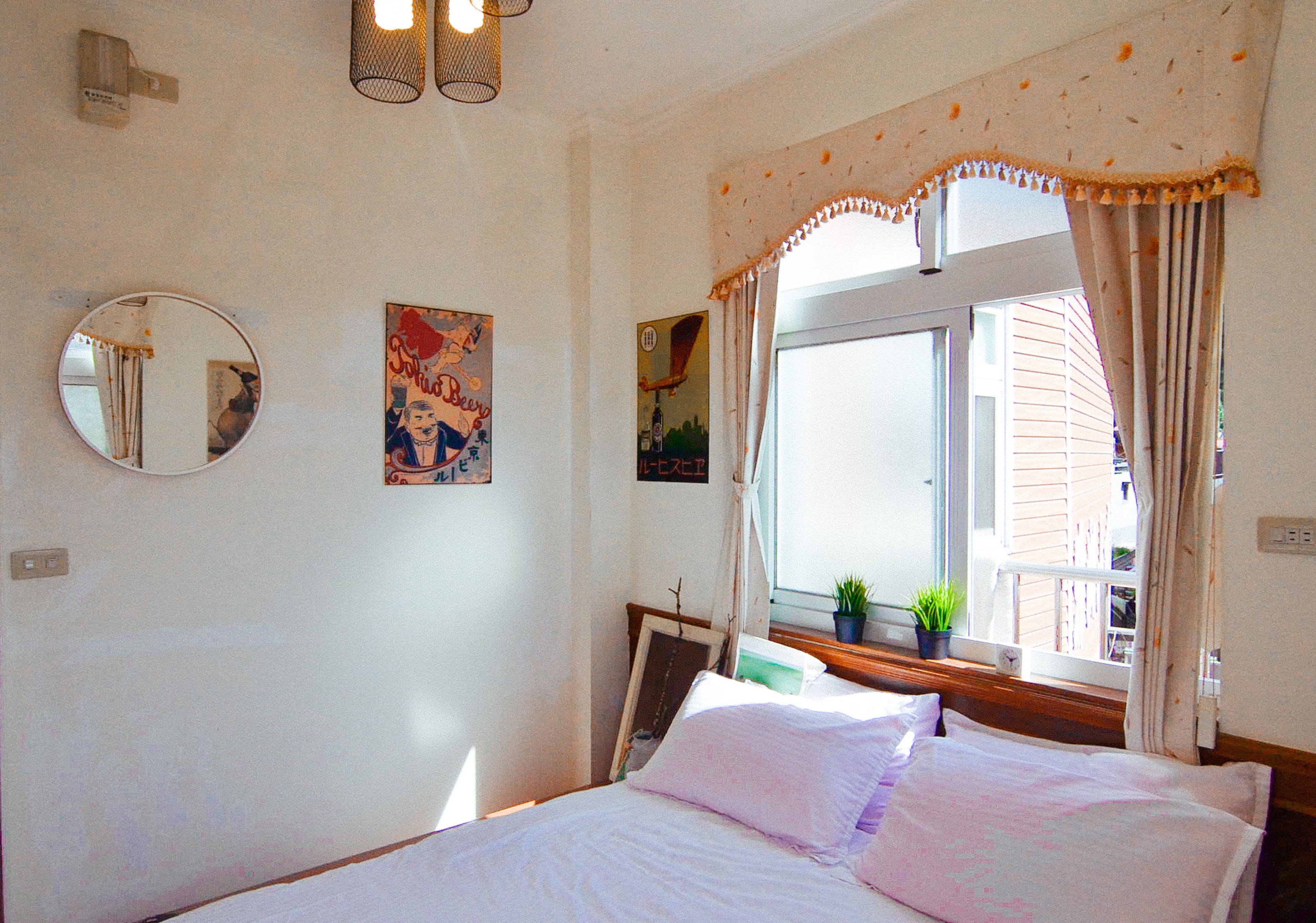Quarto com cama, espelho redondo e janela com cortinas.