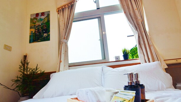 A hotel room with a bed, a tray with toiletries, a window with curtains, a potted plant, and a wall decoration. - Yahu Hotel (Zhuqi)