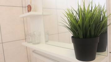 A bathroom with a white countertop, a potted plant, and a glass shower enclosure.