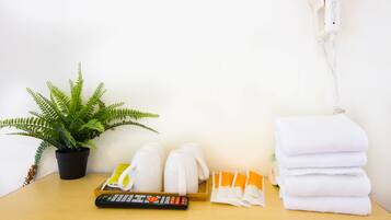 A hotel room with a potted plant, a remote control, towels, and toiletries on the table.