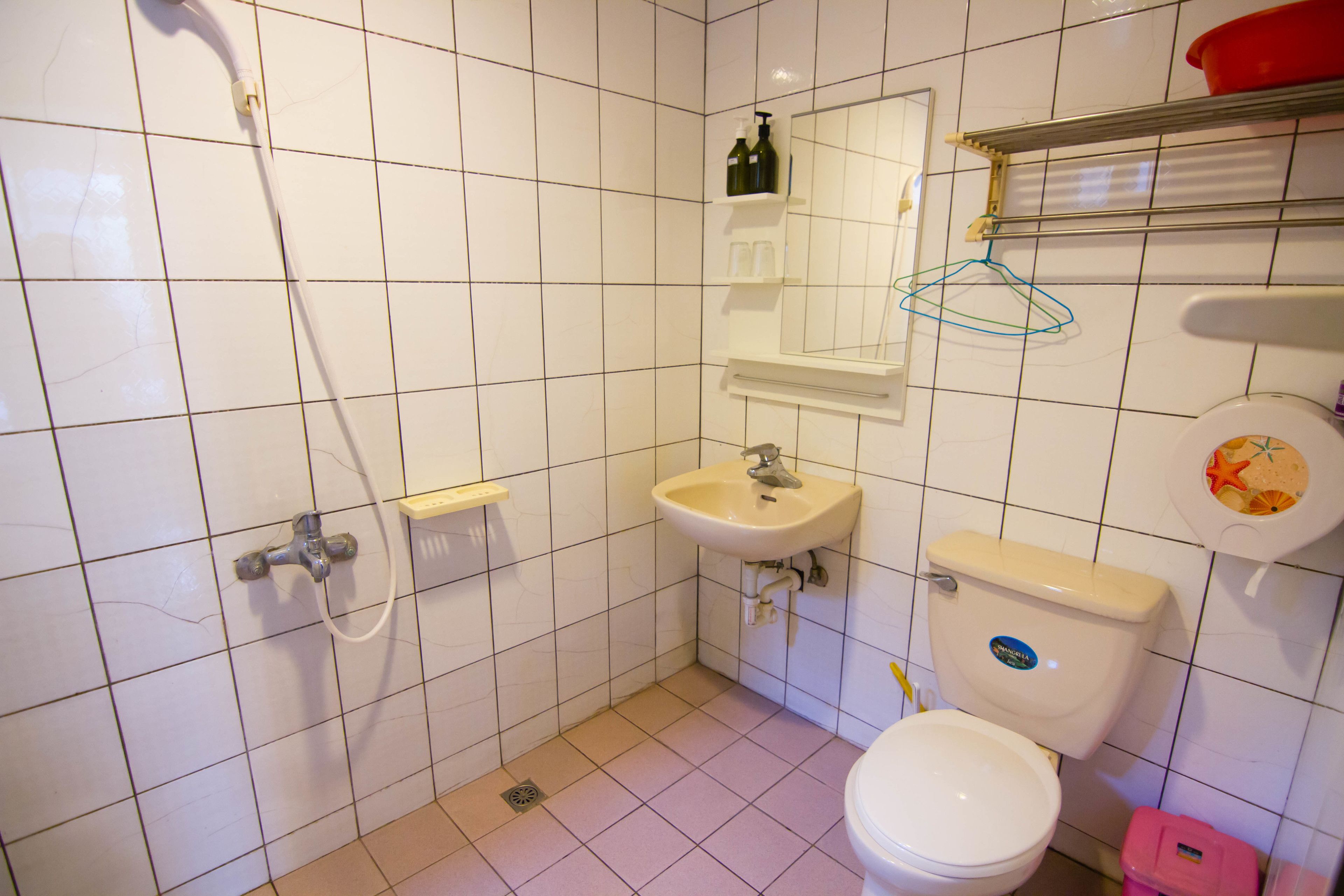 A bathroom with white tiles, a sink, a toilet, and a shower.
