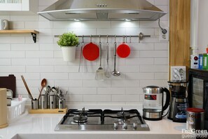 Una cocina moderna con estufa a gas, electrodomésticos de acero inoxidable, ollas colgantes y una cafetera.