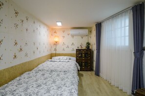 Una habitación con dos camas, una lámpara de pie, aire acondicionado y una ventana con cortinas.