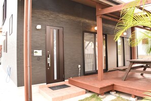 A modern building with a dark exterior, a wooden deck, and a door with a glass panel.