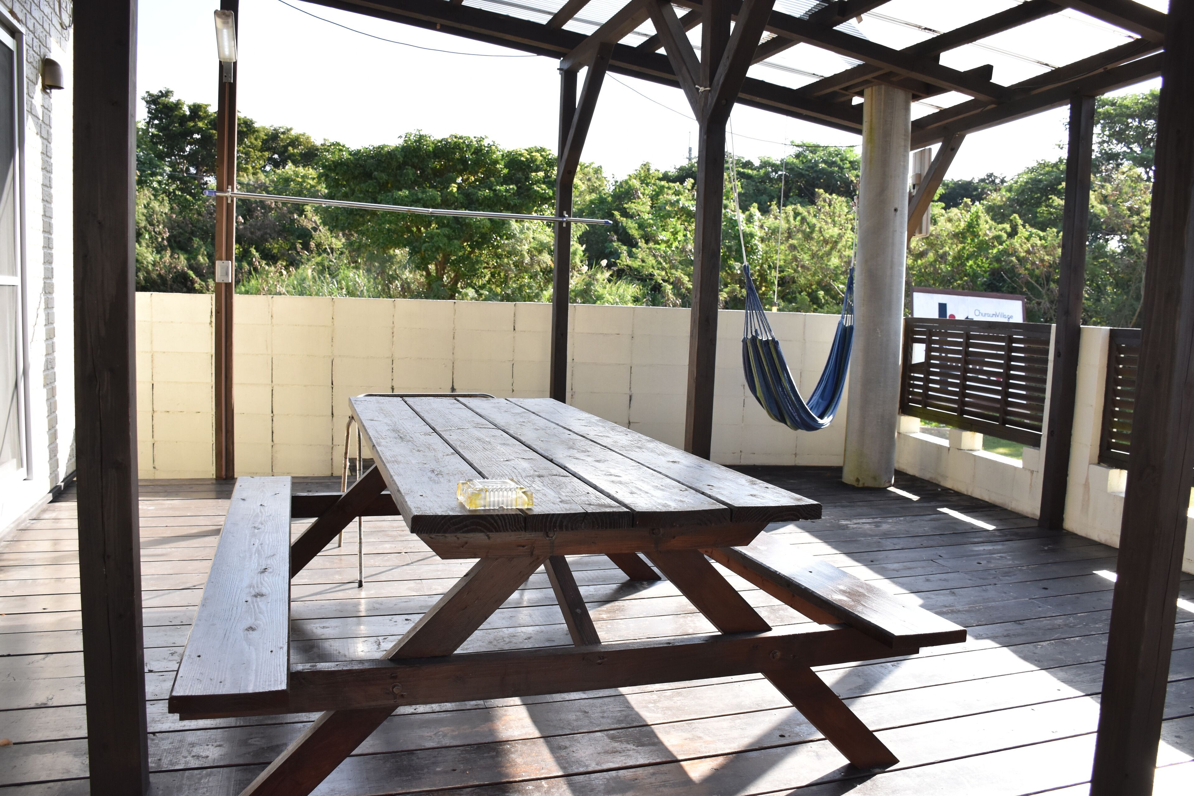 A wooden picnic table with a bottle on it, under a wooden pergola with a hammock.