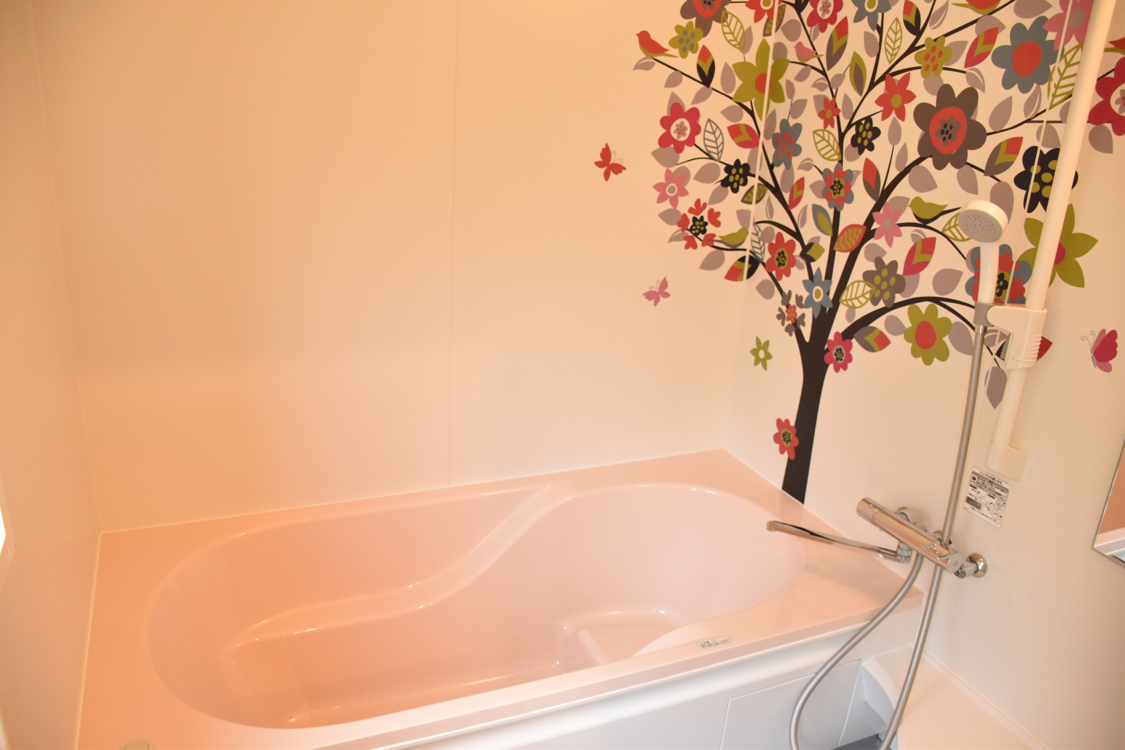 A bathtub with a shower attachment, a wall-mounted tree decal, and a faucet.