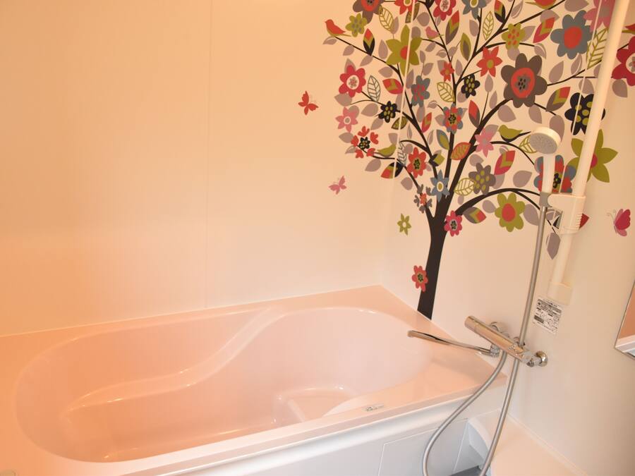 A bathtub with a shower attachment, a wall-mounted tree decal, and a faucet.