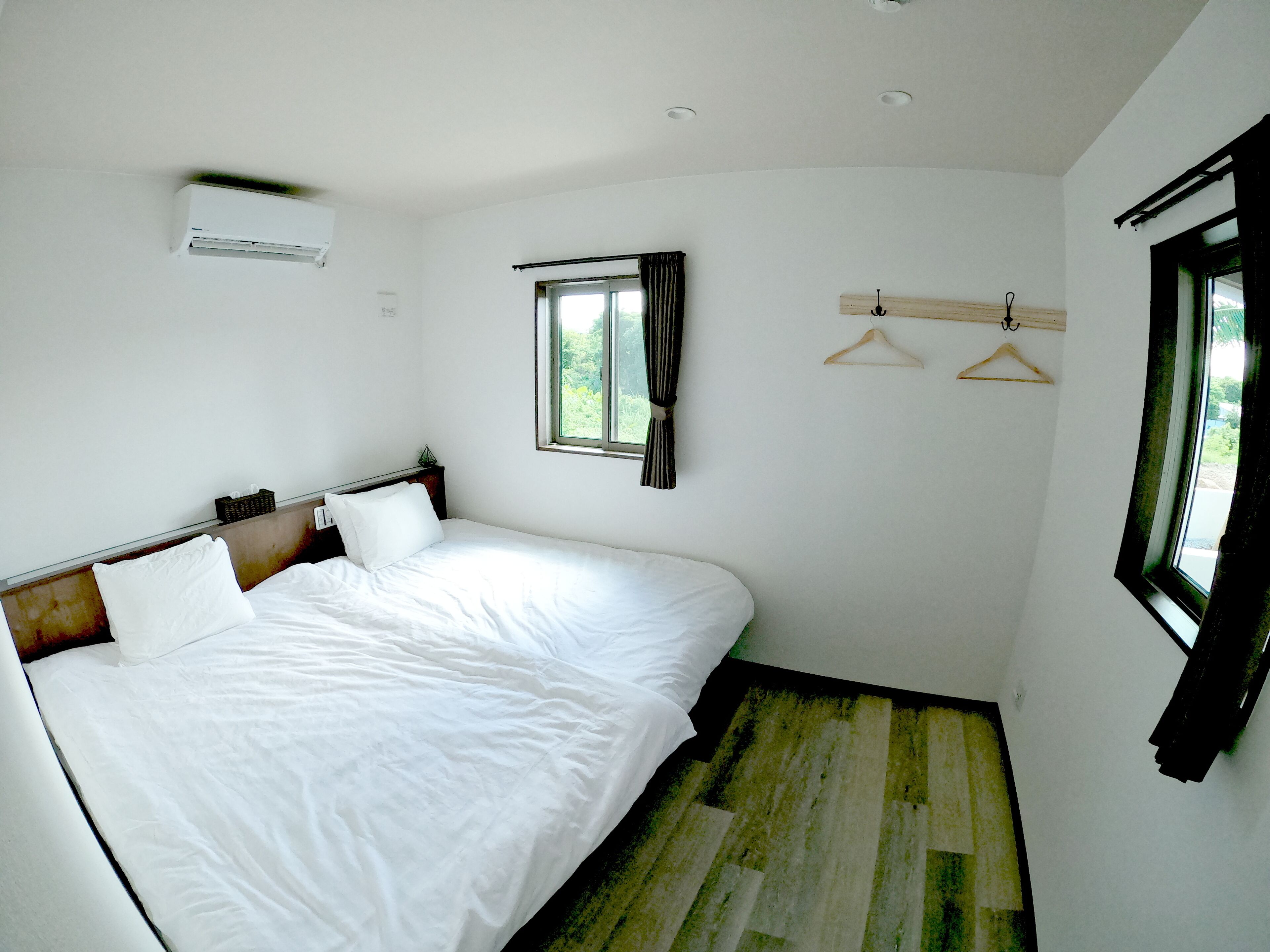 Ein Schlafzimmer mit einem großen Bett, einem Fenster, einer Wand-Klimaanlage und Holzboden.