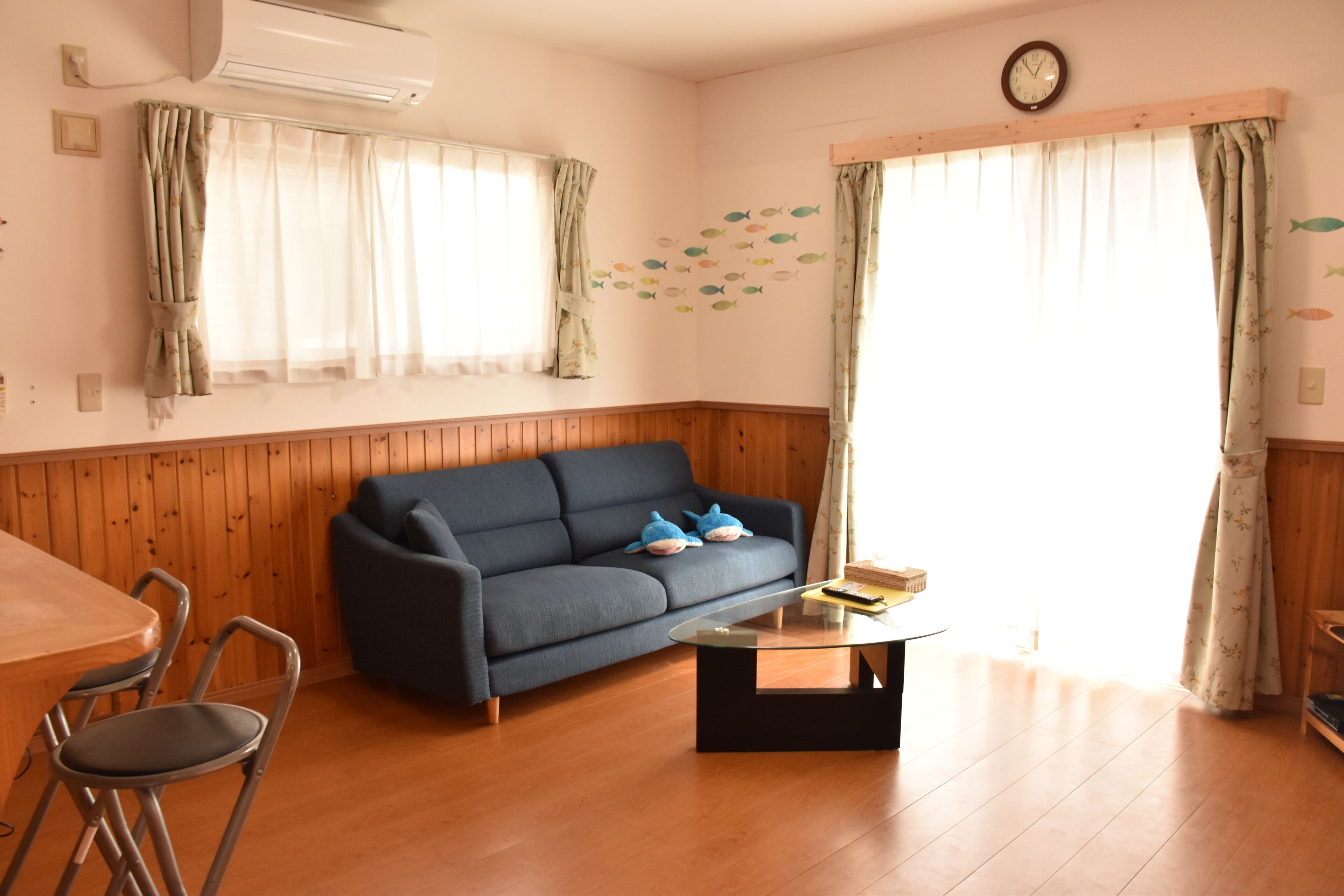 Una sala de estar con un sofá azul, una mesa de centro de vidrio y piso de madera.