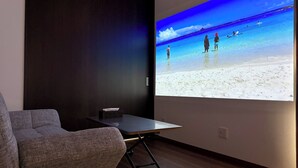 Ein Raum mit einer Projektionsleinwand, die eine Strandansicht zeigt, einem grauen Sofa und einem kleinen Tisch mit einer Taschentuchbox.