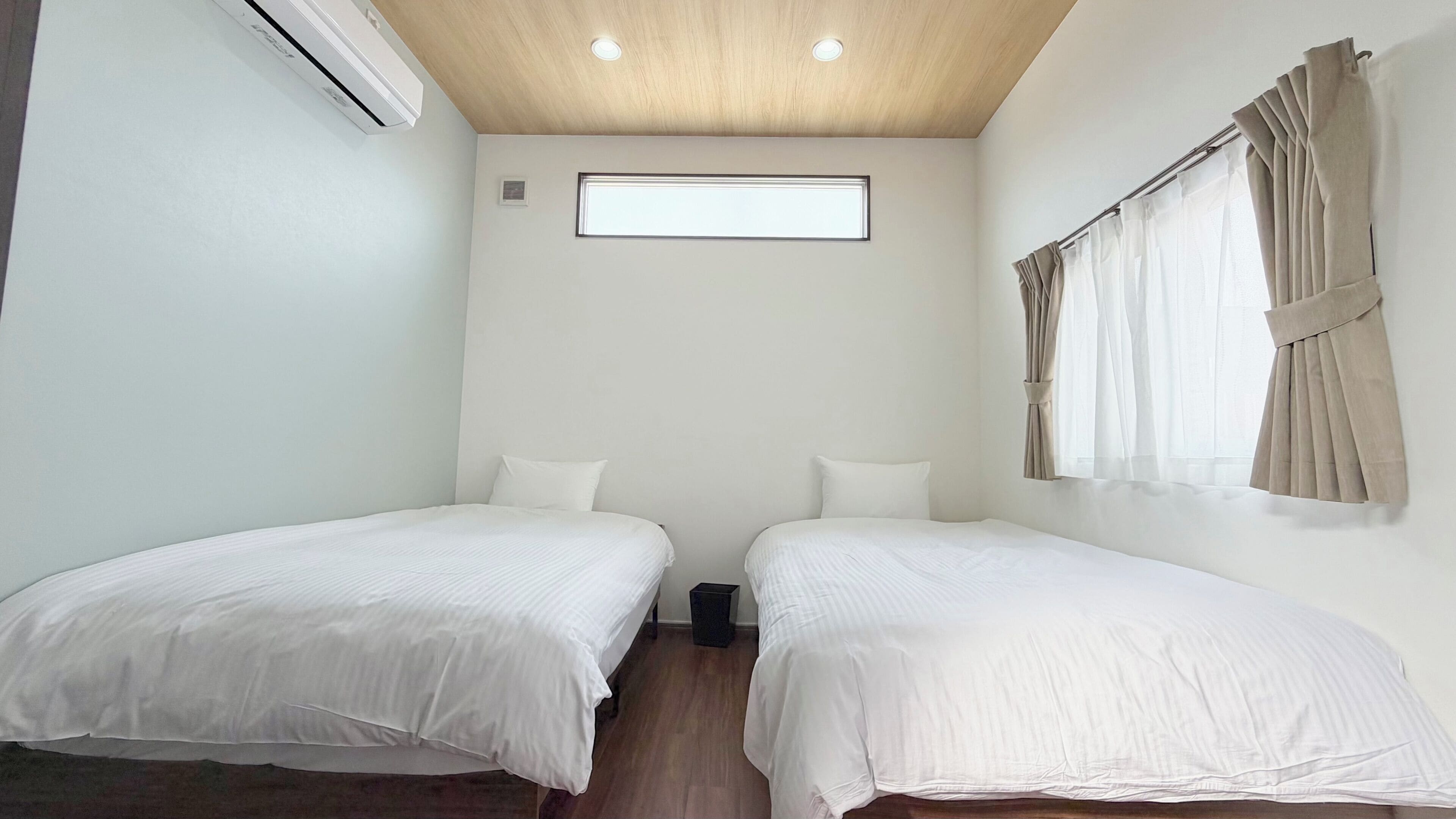 Une chambre avec deux lits, une fenêtre avec des rideaux, un appareil de climatisation et un luminaire au plafond.