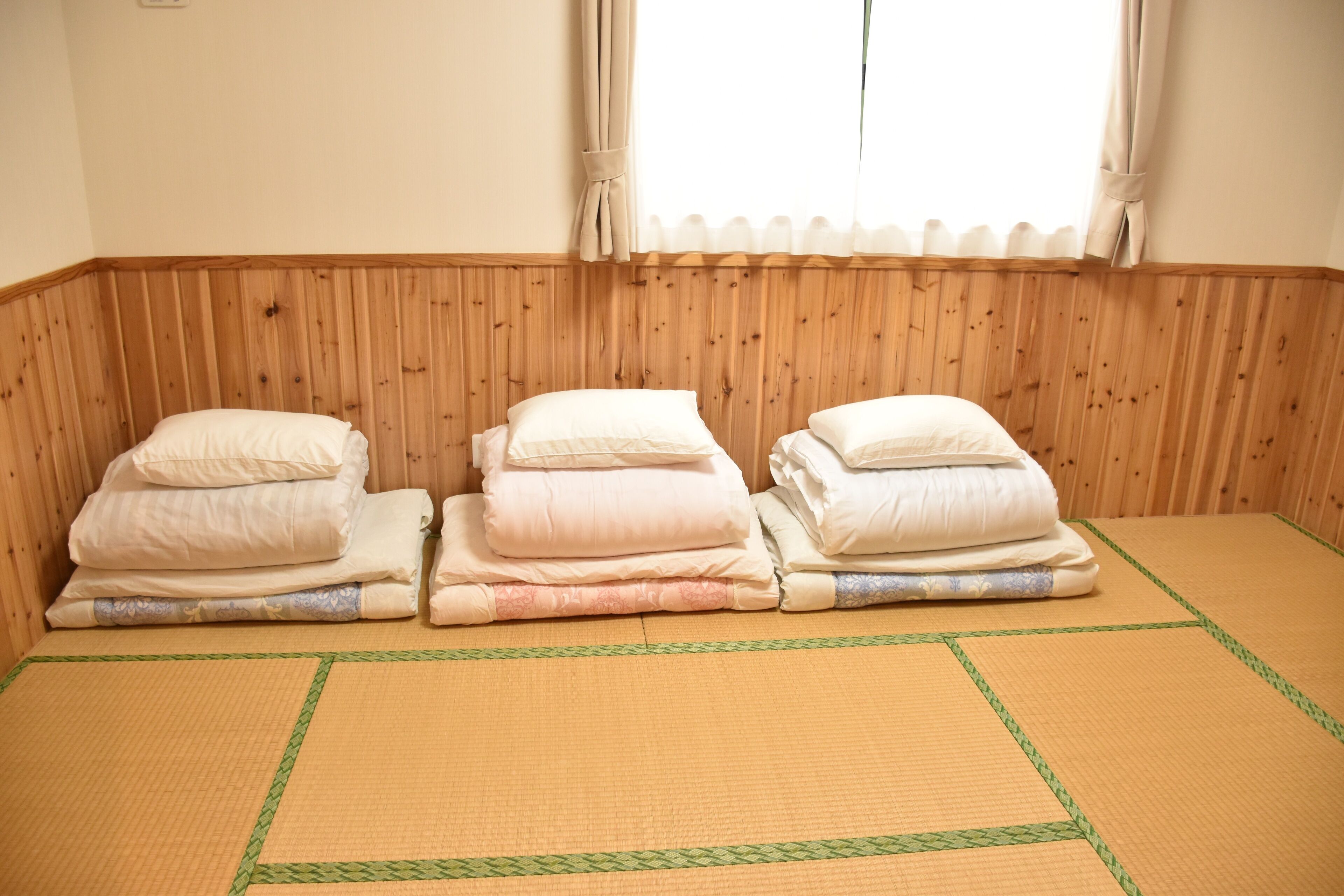 A room with a tatami mat floor, wooden paneling on the walls, and three neatly folded beds with pillows.
