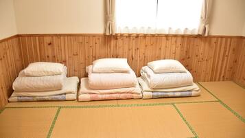 A room with a tatami mat floor, wooden paneling on the walls, and three neatly folded beds with pillows.