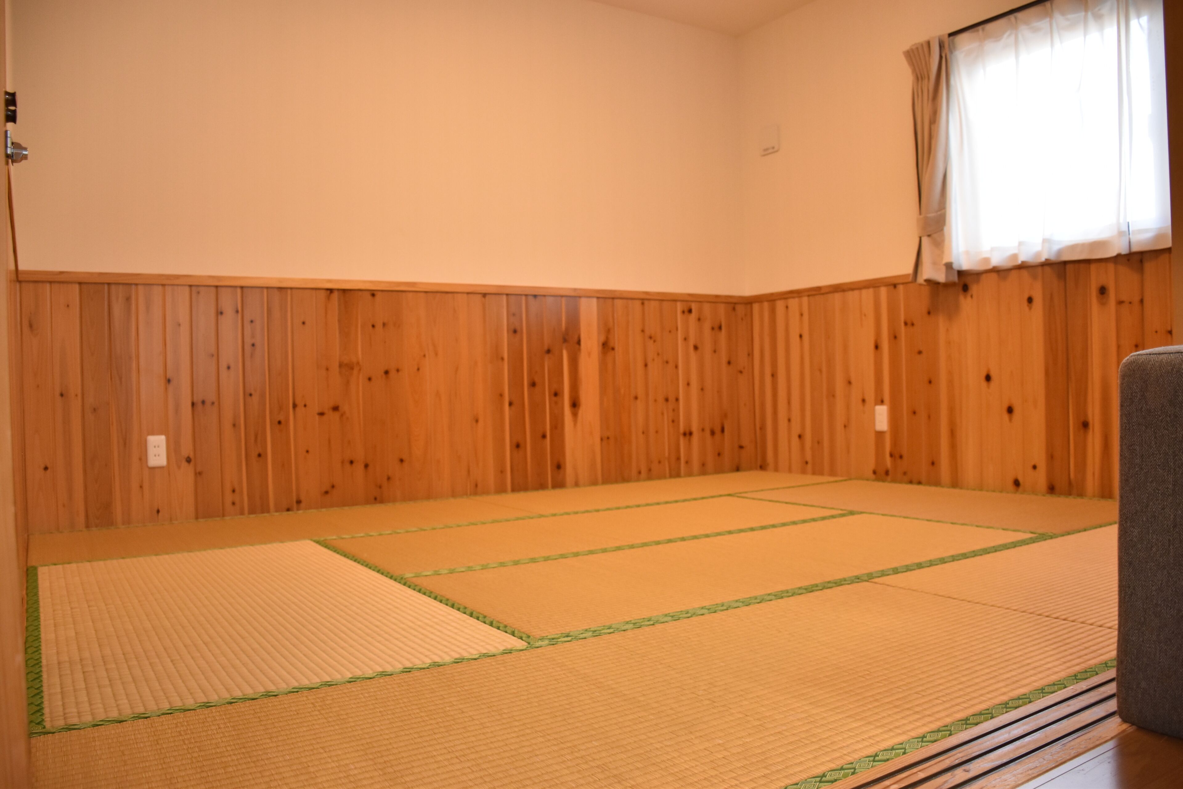 A tatami mat room with wooden panel walls and a window with curtains.