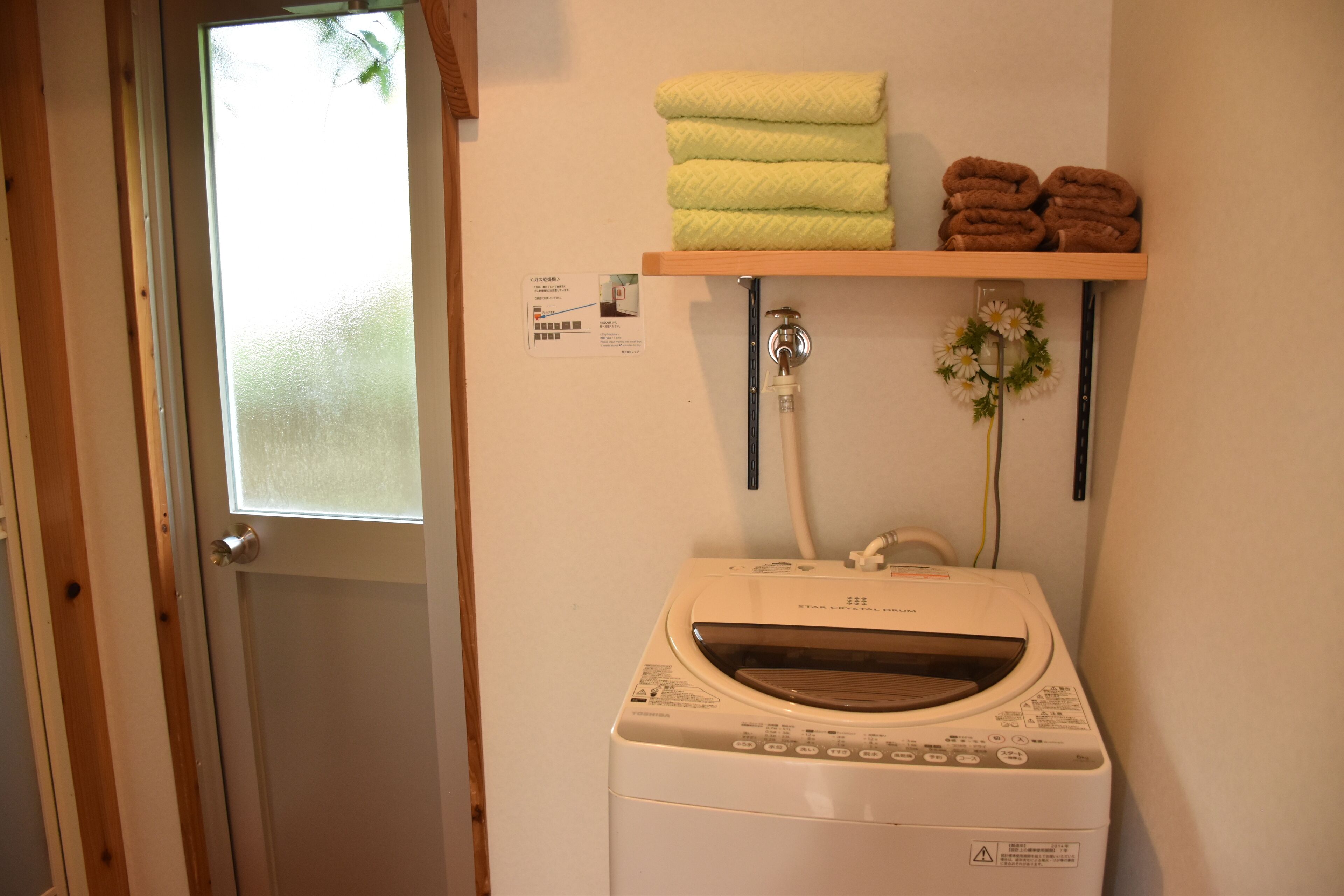 A laundry area with a washing machine, a shelf with folded towels, and a window with frosted glass.