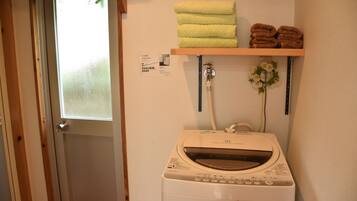 A laundry area with a washing machine, a shelf with folded towels, and a window with frosted glass.