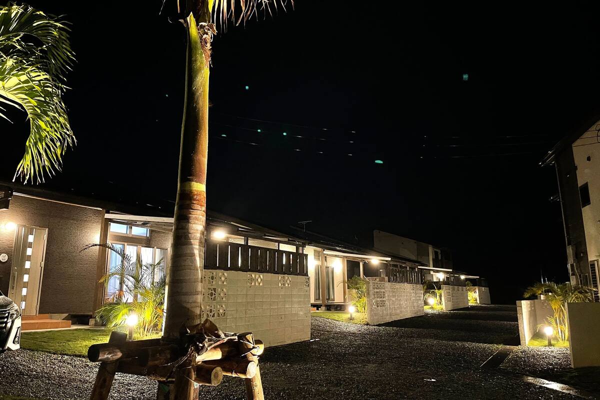 Un edifici modern amb entrada ben il·luminada, una palmera i un carrer d'accés de grava.