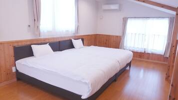 Un grand lit dans une chambre aux murs lambrissés, une fenêtre avec des rideaux et un appareil de climatisation.