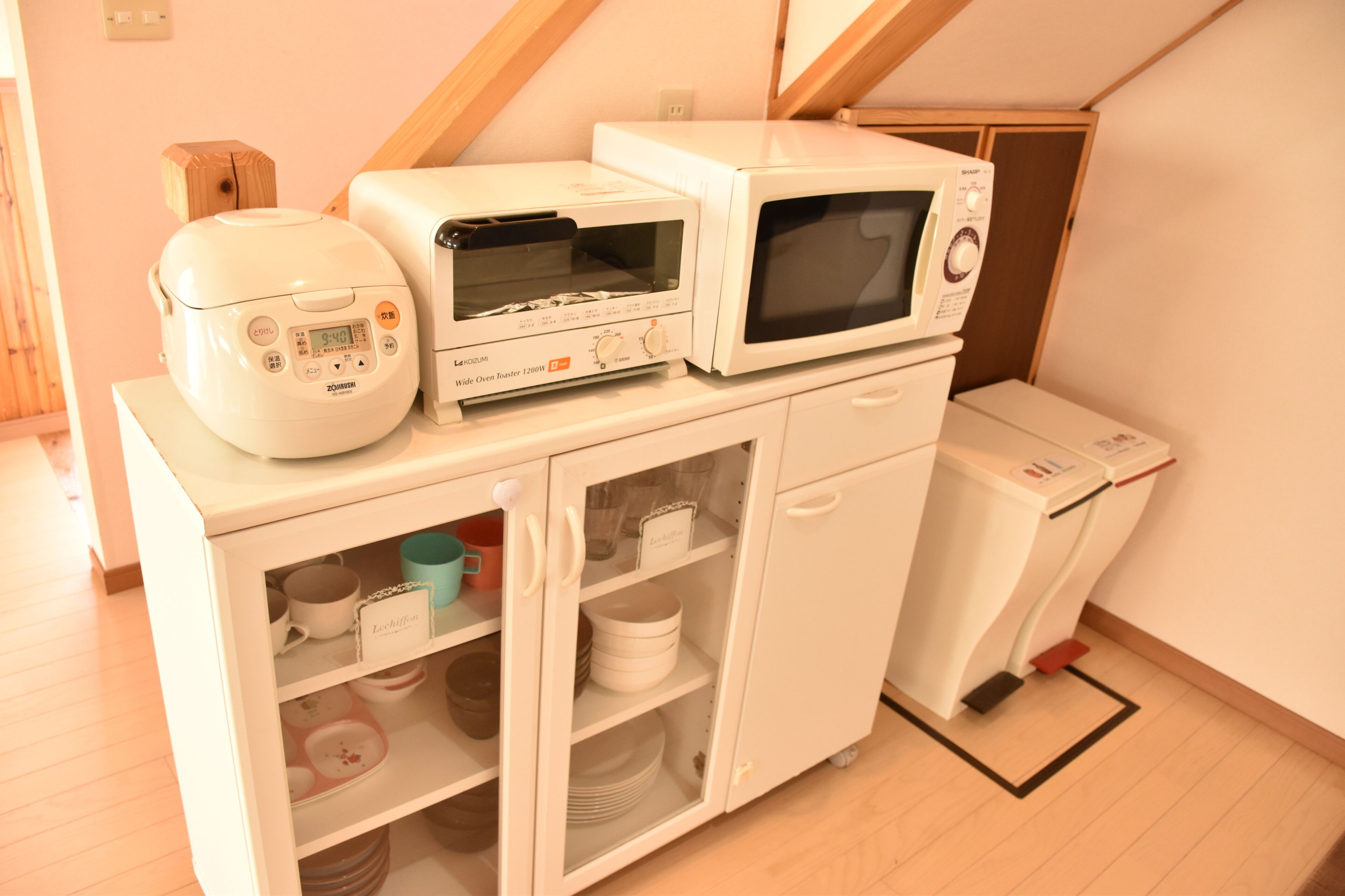 Una kitchenette compacta con microondas, tostadora y cocedor de arroz sobre una pequeña encimera.