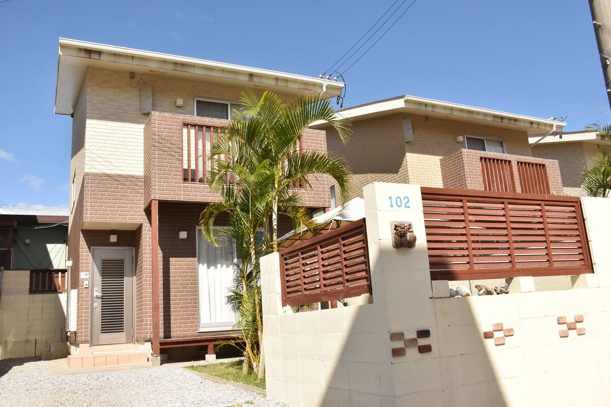 Edifici residencial de dues plantes amb façana de maó, entrada tancada per reixes i una palmera al jardí davanter.