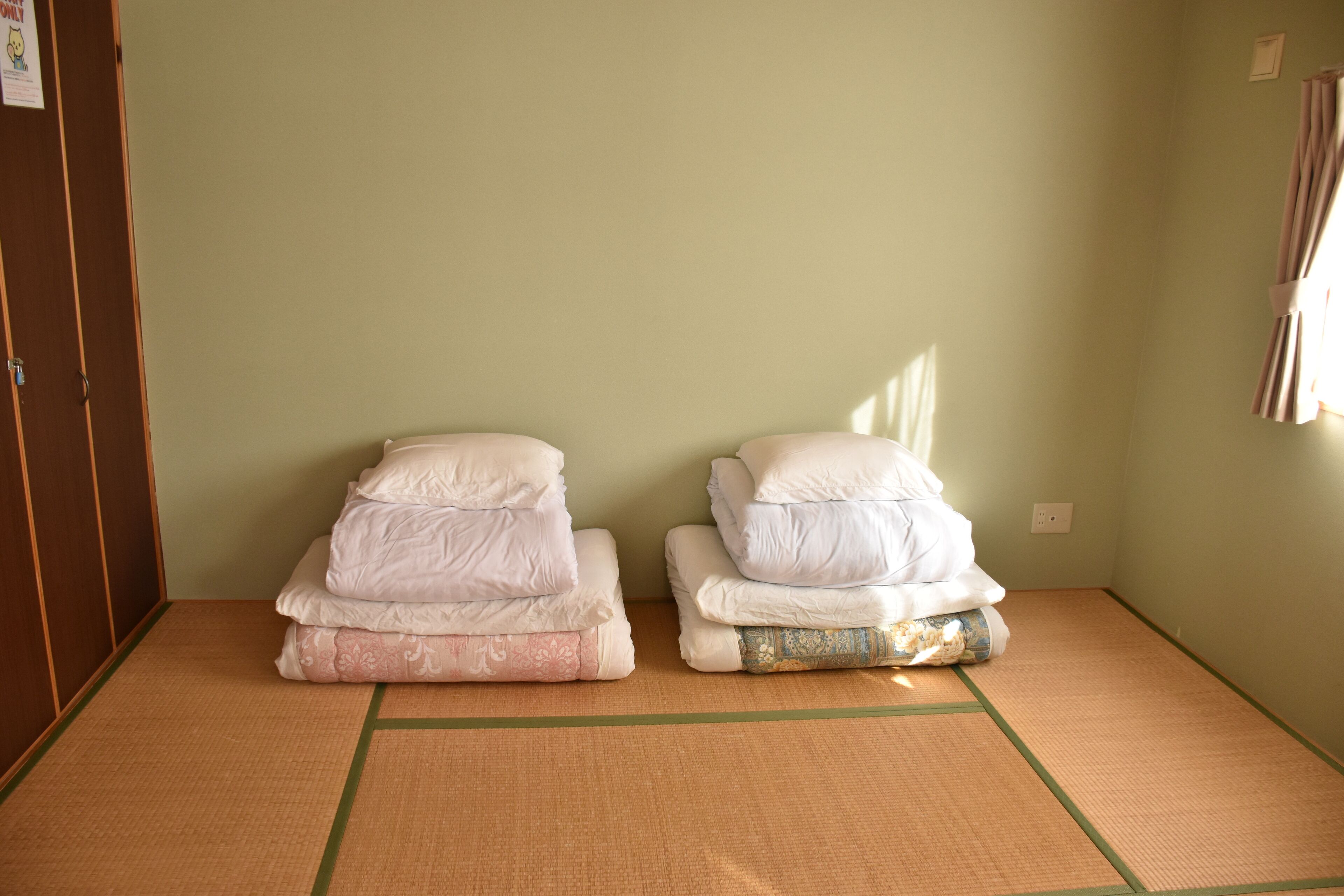 A room with two beds, a tatami mat floor, and a green wall.