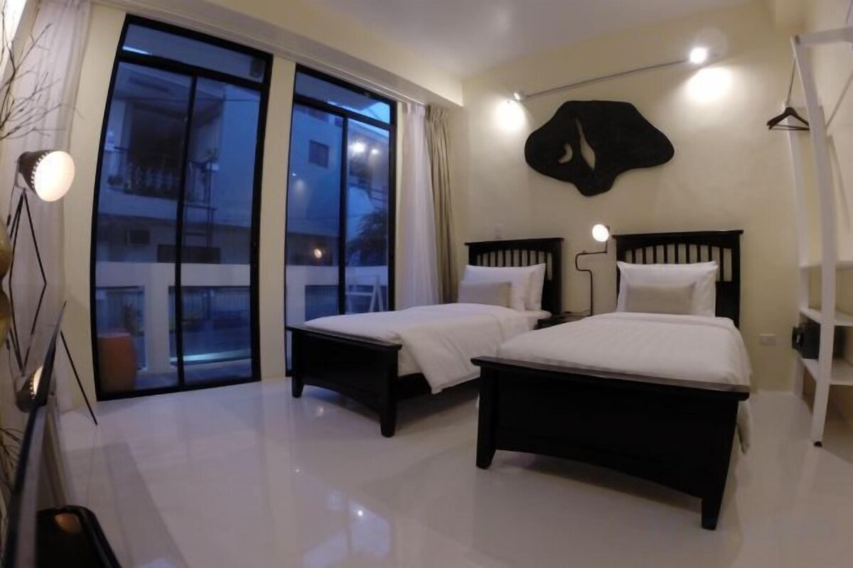 A bedroom with two beds, a large window, and a hanging coat rack.