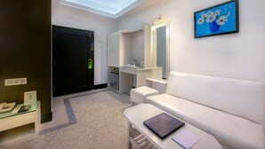 A hotel room with a skylight, a white sofa, a small table with a notebook, a mirror, and a painting of flowers on the wall. - Treebo Green View, Park Circus (Kolkata)