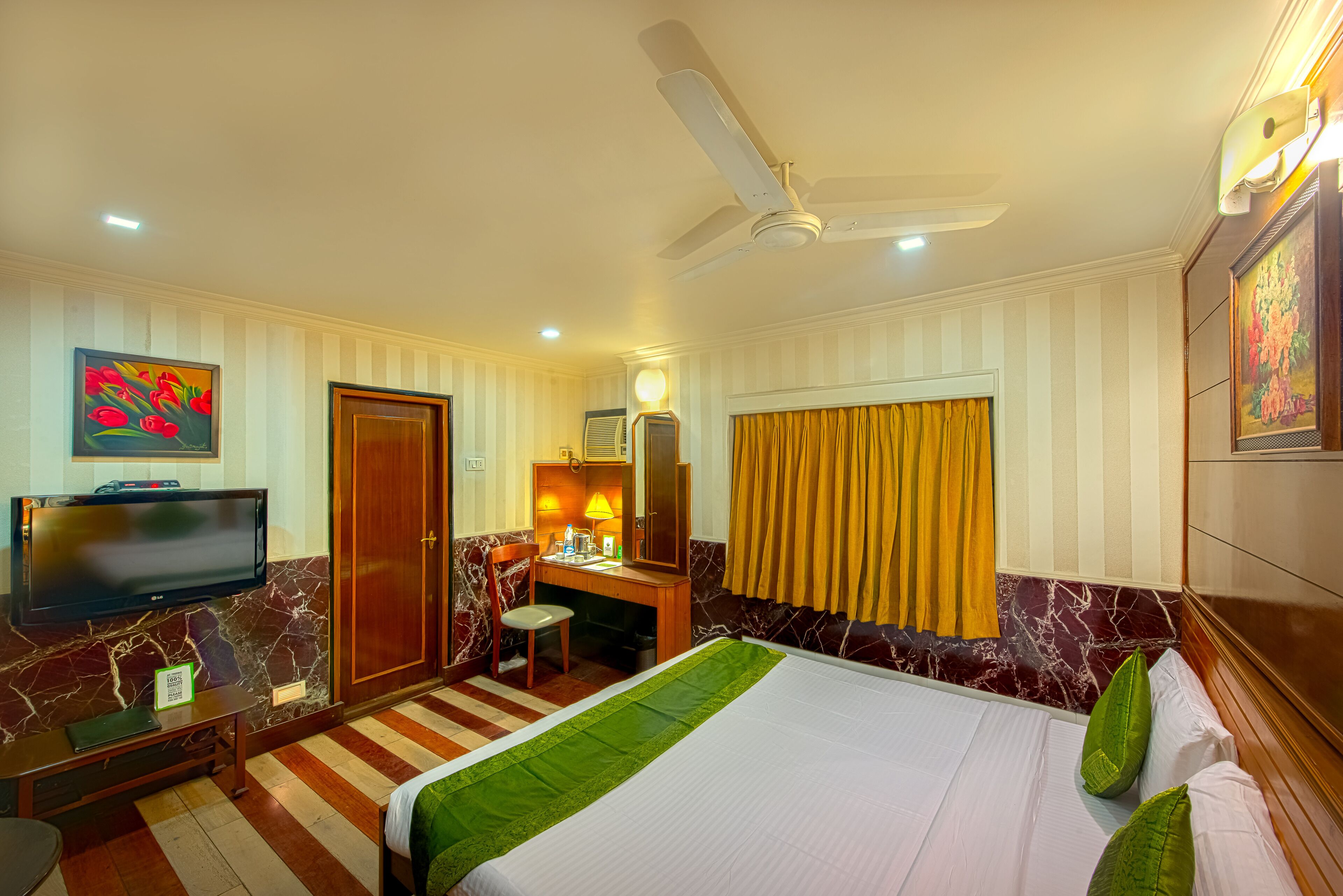 A hotel room with a bed, a desk, a chair, a television, and a ceiling fan.