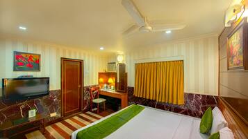 A hotel room with a bed, a desk, a chair, a television, and a ceiling fan.