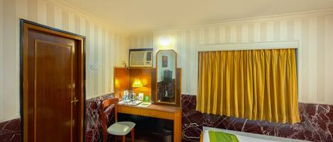 Habitación de hotel con escritorio de madera, una silla, cama, armario y ventana con cortinas.
