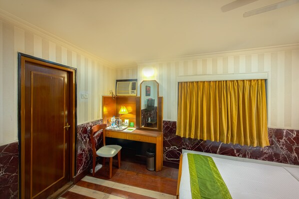 Une chambre d’hôtel avec un bureau en bois, une chaise, un lit, une armoire et une fenêtre avec des rideaux.