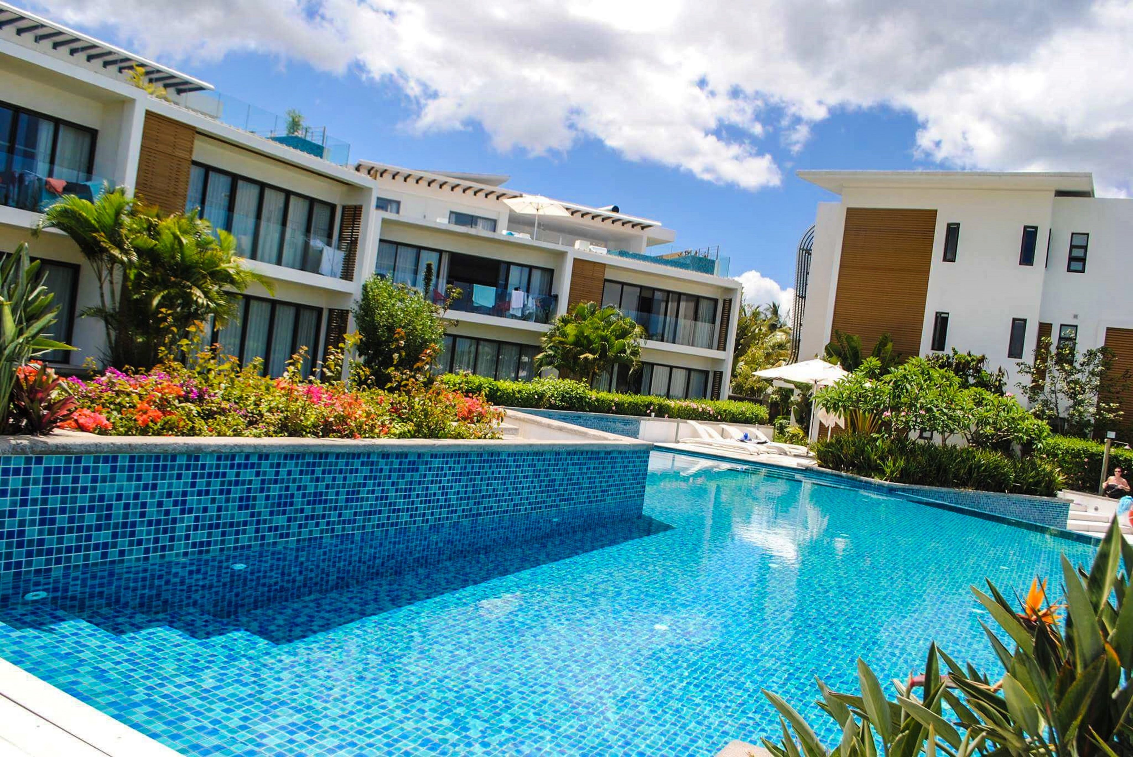 A modern hotel with a swimming pool, multiple balconies, and lush landscaping.