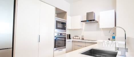 A modern kitchen with white cabinetry, a stainless steel refrigerator, an oven, a microwave, a sink, and a faucet.