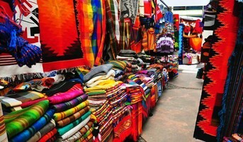 Puesto de mercado con diversos textiles y telas de colores exhibidos para la venta.