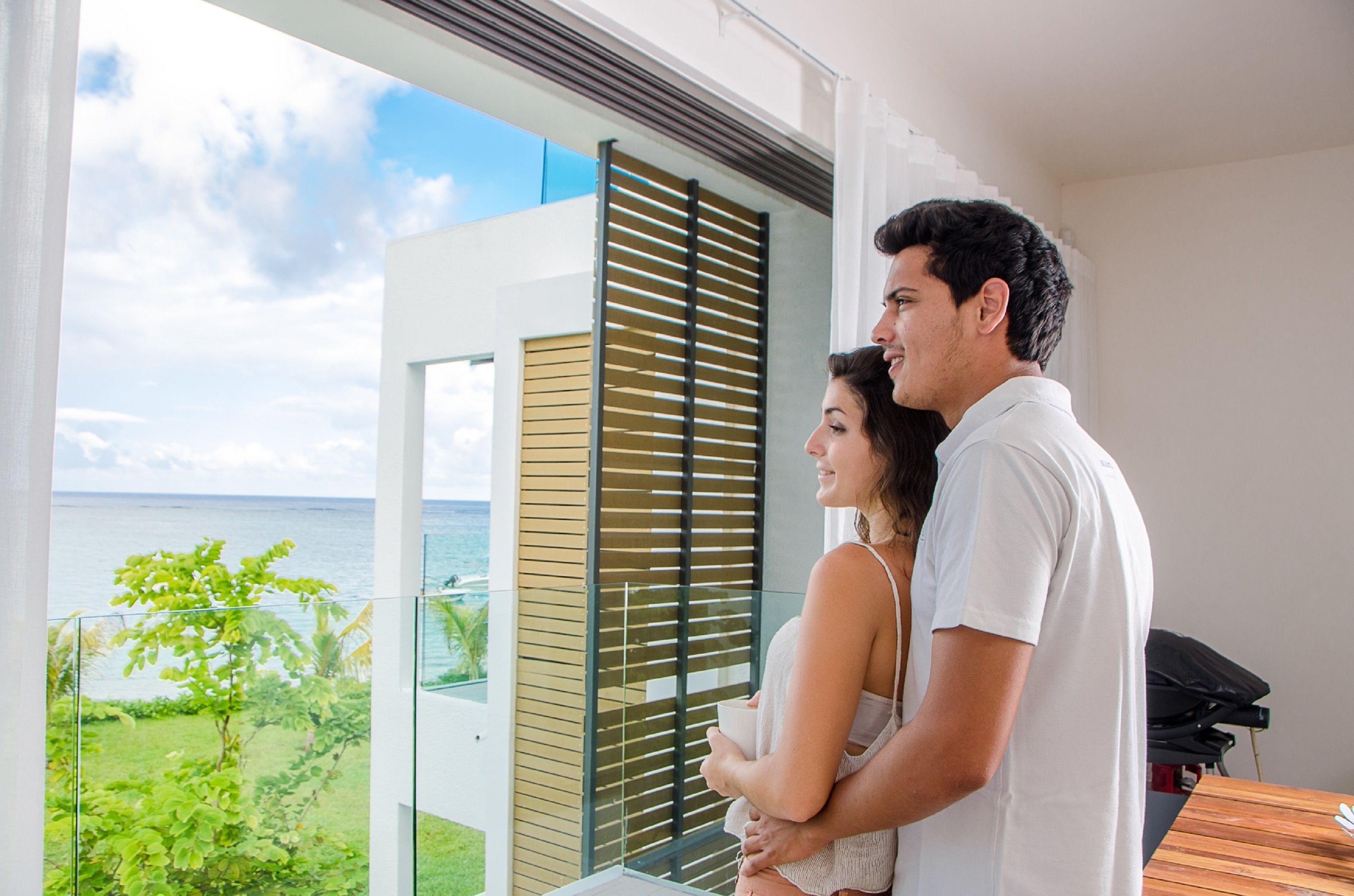 A couple standing by a balcony with a view of the ocean.