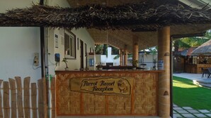 A reception area with a wooden sign reading "Parrot Resort Reception," a thatched roof, and a fenced garden. - Parrot Resort Moalboal (Moalboal)