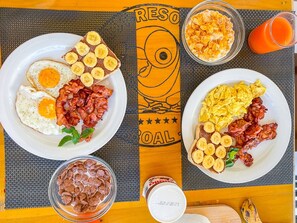 A breakfast table with plates of eggs, bacon, and pancakes, a bowl of cereal, and a glass of orange juice. - Parrot Resort Moalboal (Moalboal)