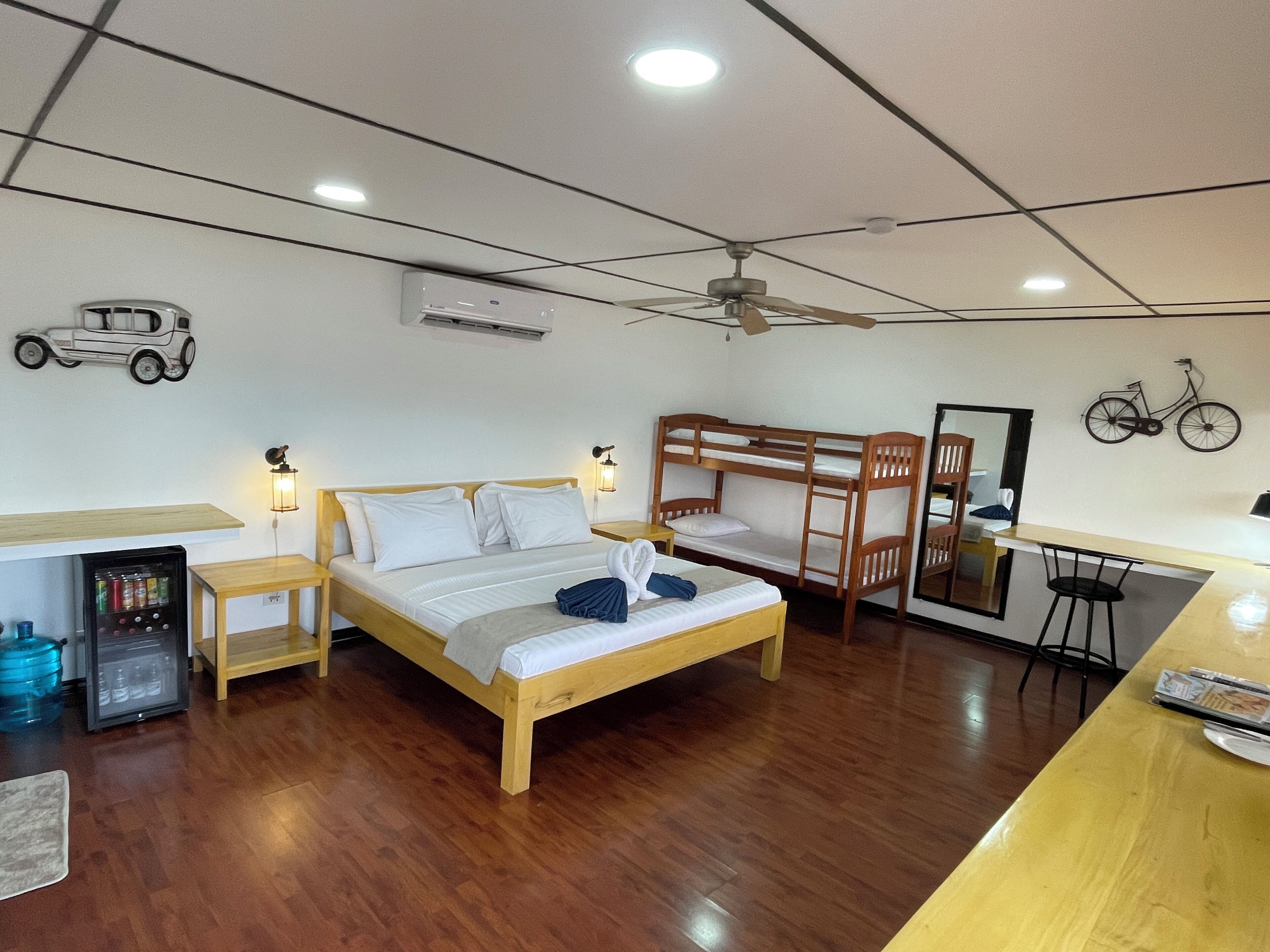 A room with a bunk bed, a desk, a chair, a refrigerator, a mirror, and a ceiling fan.