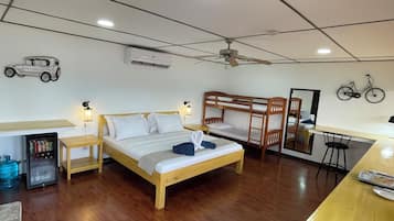 A room with a bunk bed, a desk, a chair, a refrigerator, a mirror, and a ceiling fan.