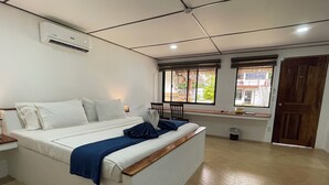 A hotel room with a large bed, a window with a view, a wooden door, and a trash bin. - Parrot Resort Moalboal (Moalboal)